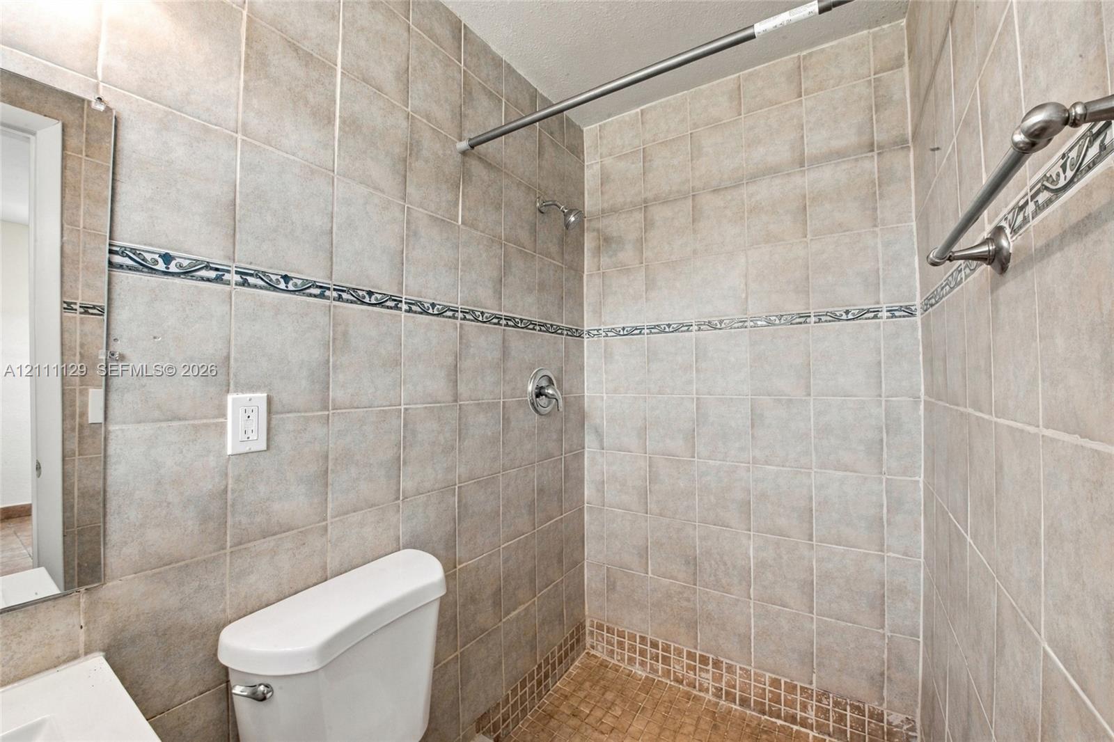 Walk-in shower featuring floor-to-ceiling neutral ceramic tiling, decorative accent border, mosaic tile floor, and metallic shower hardware