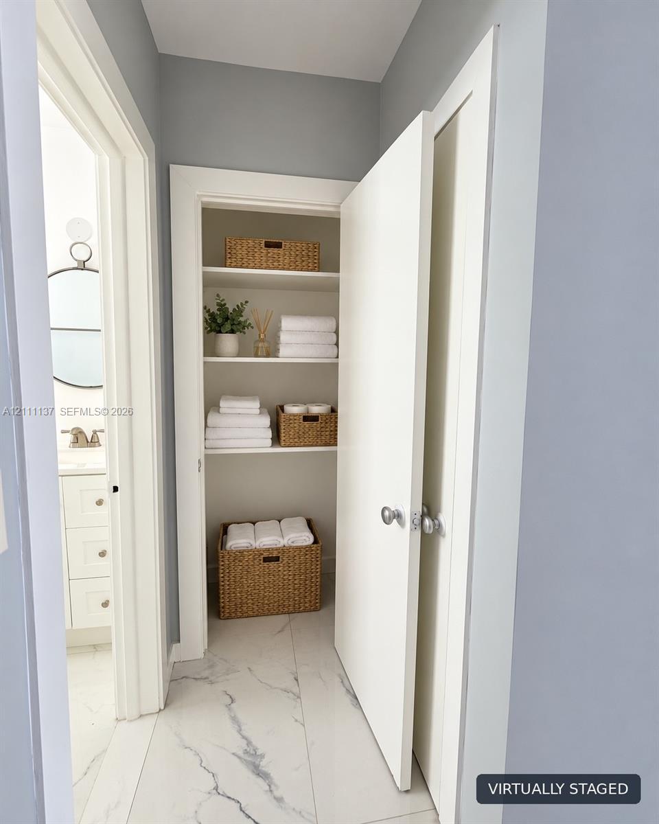 Built-in storage closet featuring multi-level shelving and white interior casing, complemented by large-format light-toned stone-finish tile flooring