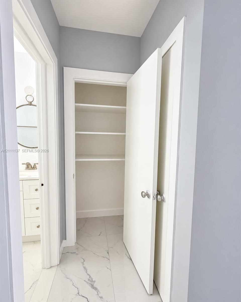 Storage closet featuring white shelving, paired with large-format light-toned flooring featuring grey veining