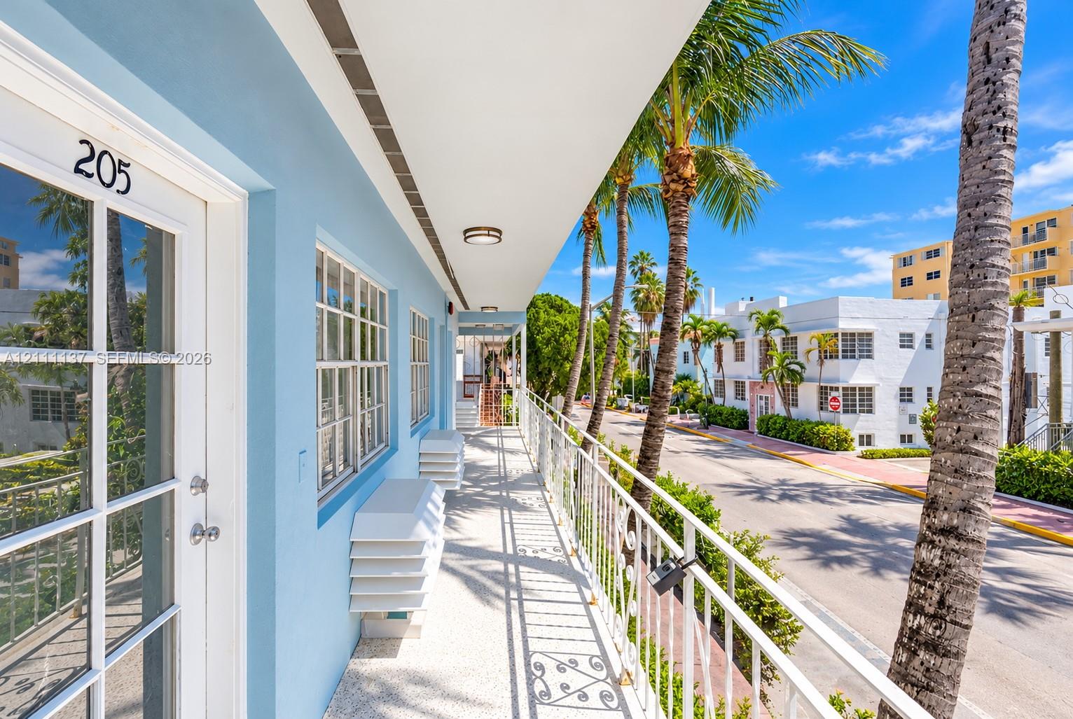 Exterior walkway featuring a painted stucco finish, multi-lite glass panel door, terrazzo flooring, metal lattice railing, and overhead recessed lighting Exterior walkway featuring a painted stucco finish, multi-lite glass panel door, terrazzo flooring, metal lattice railing, and overhead recessed lighting