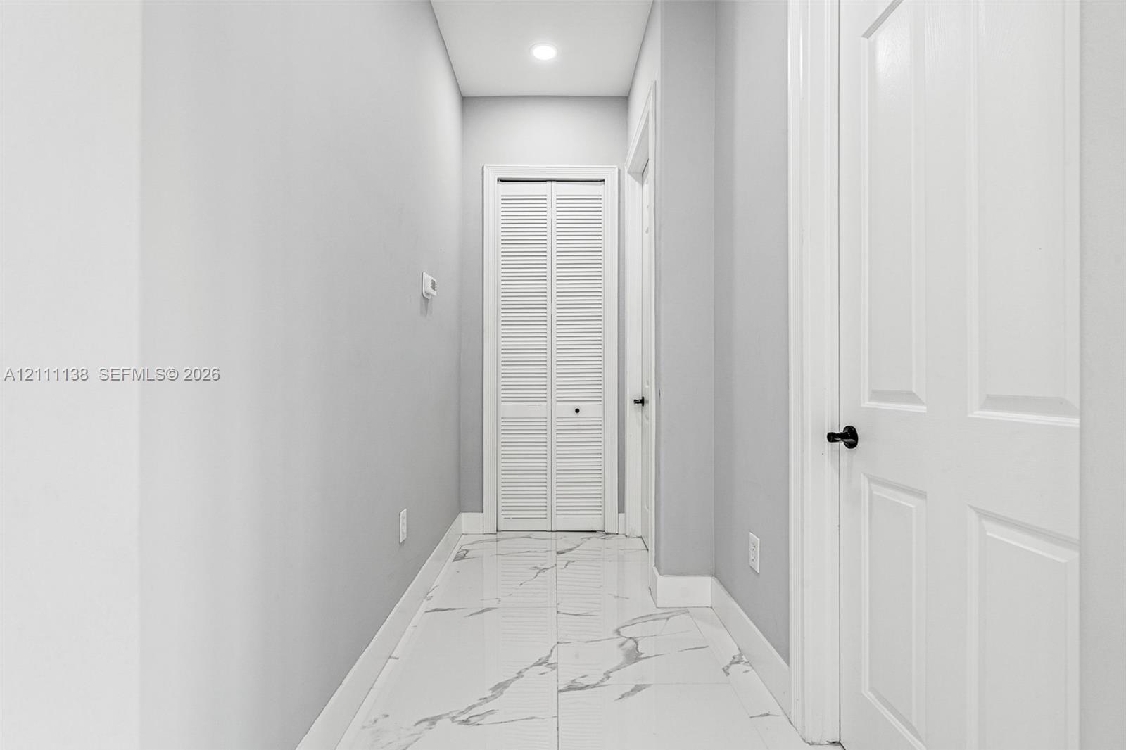 Hallway featuring polished tile flooring with a veined pattern, recessed ceiling lighting, and crisp white interior doors with matte black hardware