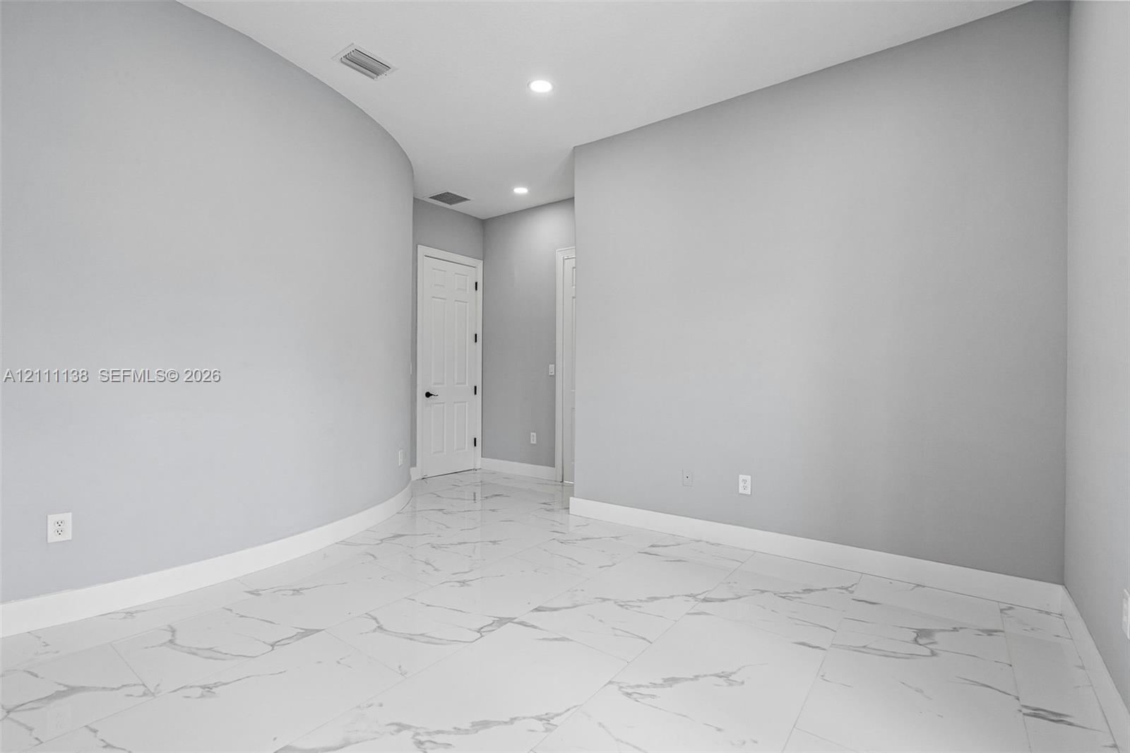 Interior space featuring polished large-format tile flooring with veining, curved wall architecture, and recessed ceiling lighting