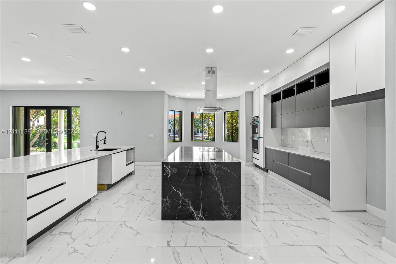 Modern kitchen featuring flat-panel cabinetry, a central island with a contrasting stone finish, stone-surface countertops, tile flooring, and a stainless steel ceiling-mounted vent hood