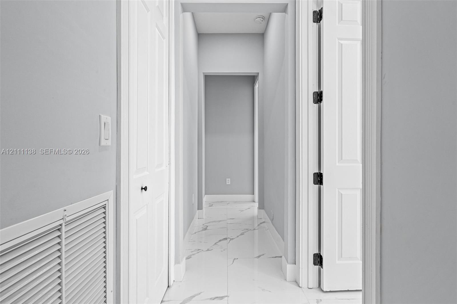 Hallway featuring white veined tile flooring, solid core two-panel doors, and neutral wall tones