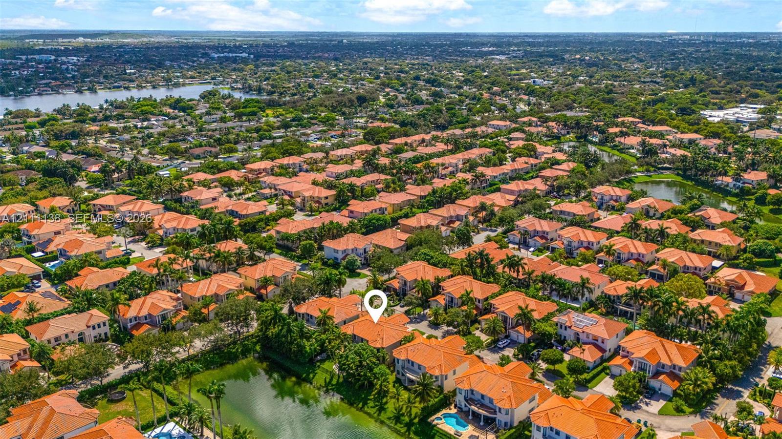 Aerial perspective highlighting a residential property featuring a tile roof, paved driveway, and proximity to neighborhood lakes and tropical landscaping