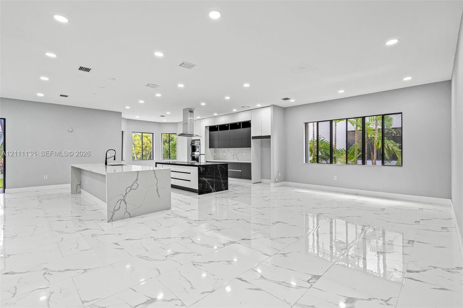 Open-concept kitchen featuring dual islands with veined stone-finish countertops, matte black plumbing fixtures, two-tone flat-panel cabinetry, and polished large-format tile flooring