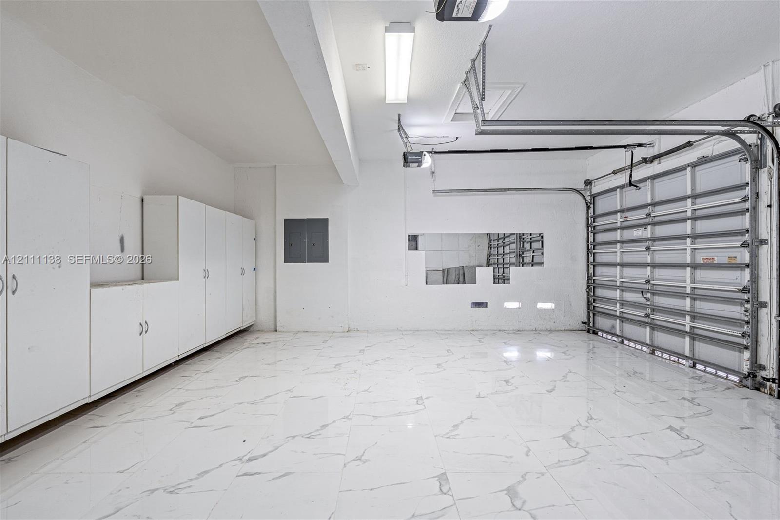 Garage featuring expansive stone-finish flooring, extensive white built-in cabinetry, overhead task lighting, and an automated sectional door