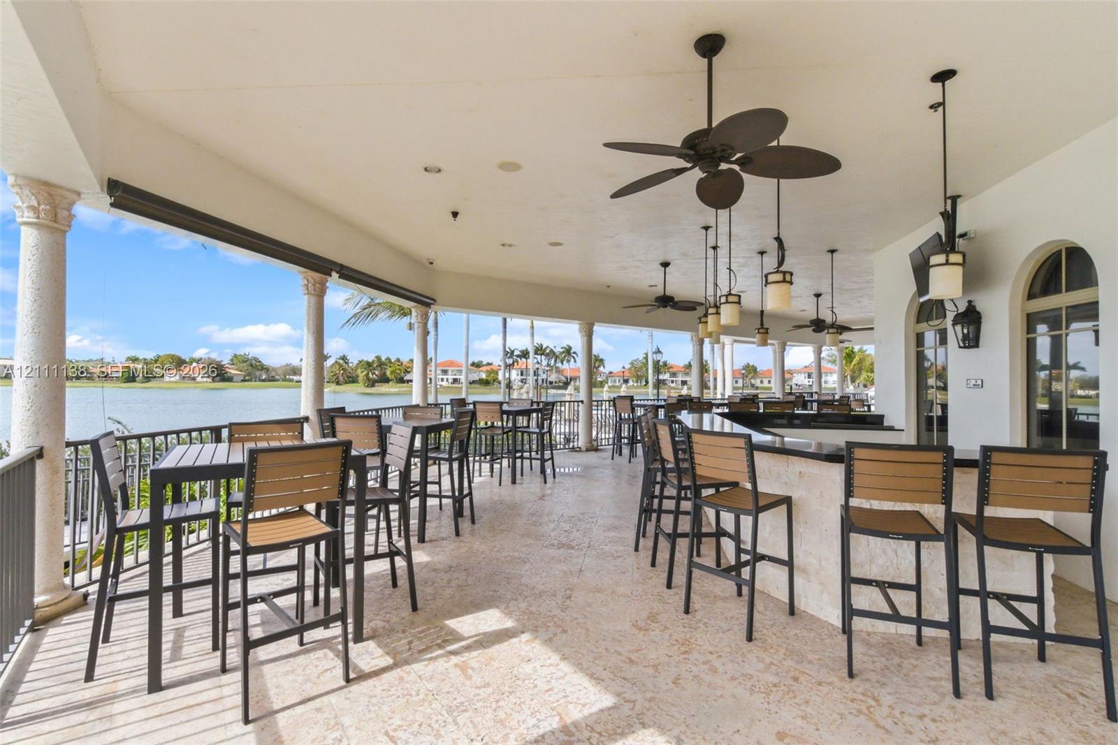 Covered patio featuring stone-finish flooring, built-in stone bar with a dark countertop, ceiling-mounted fans, decorative pendant lighting, and stone columns