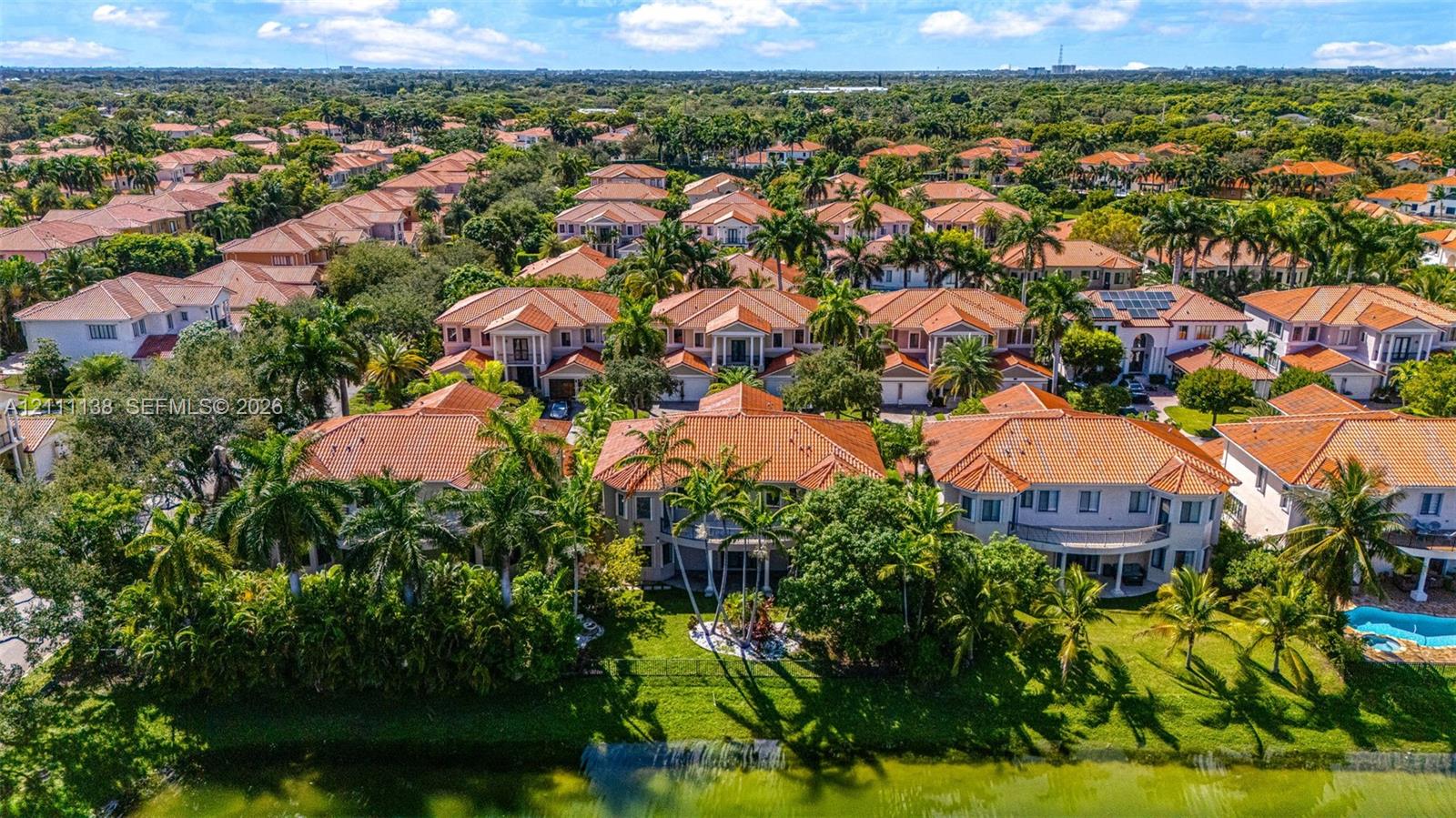 Aerial perspective featuring tile-roofed residences, landscaped grounds with mature palm trees, and waterfront perimeter