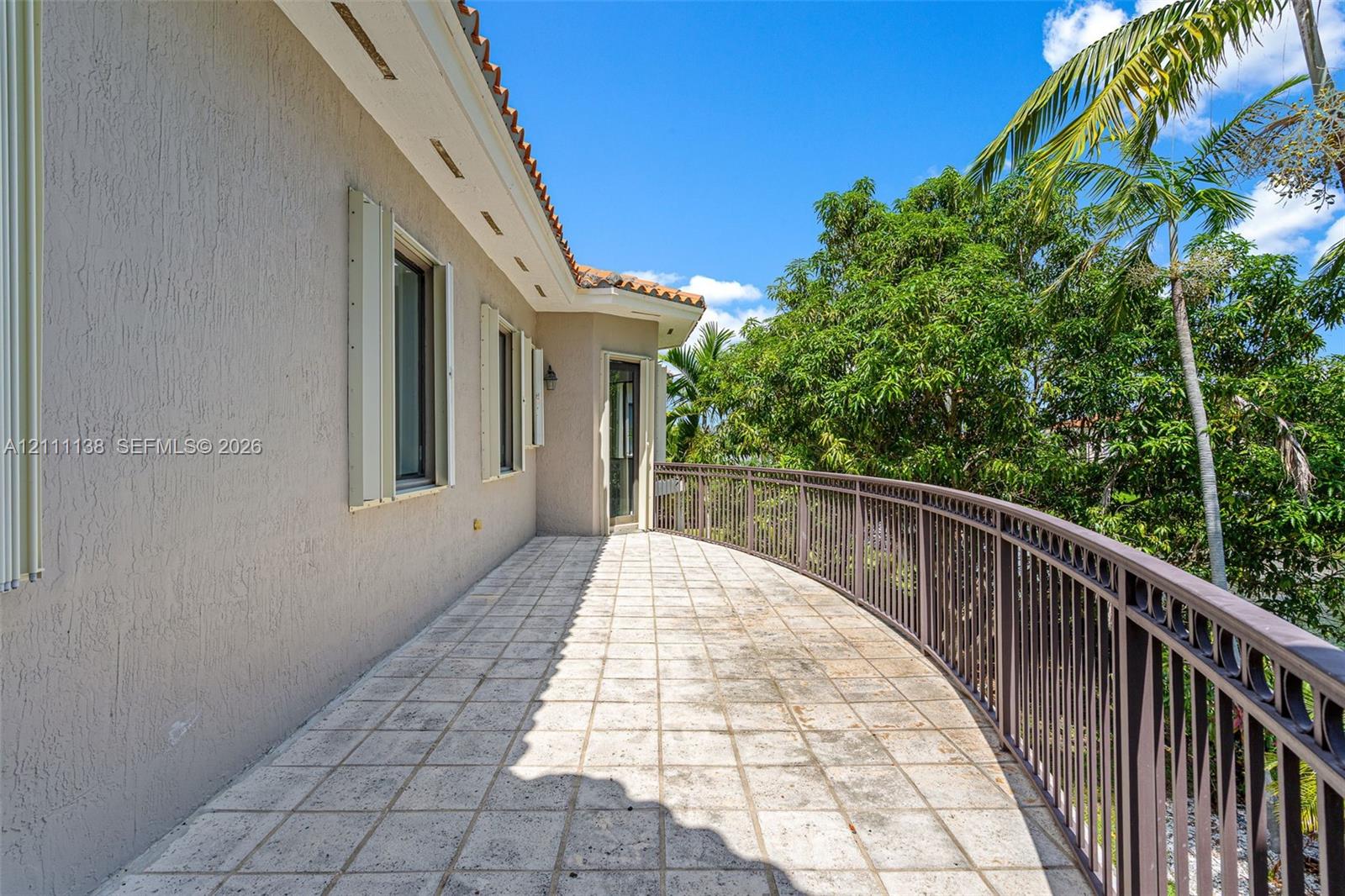 Curved exterior terrace featuring stone-finish tile flooring, a metal railing, and stucco wall construction