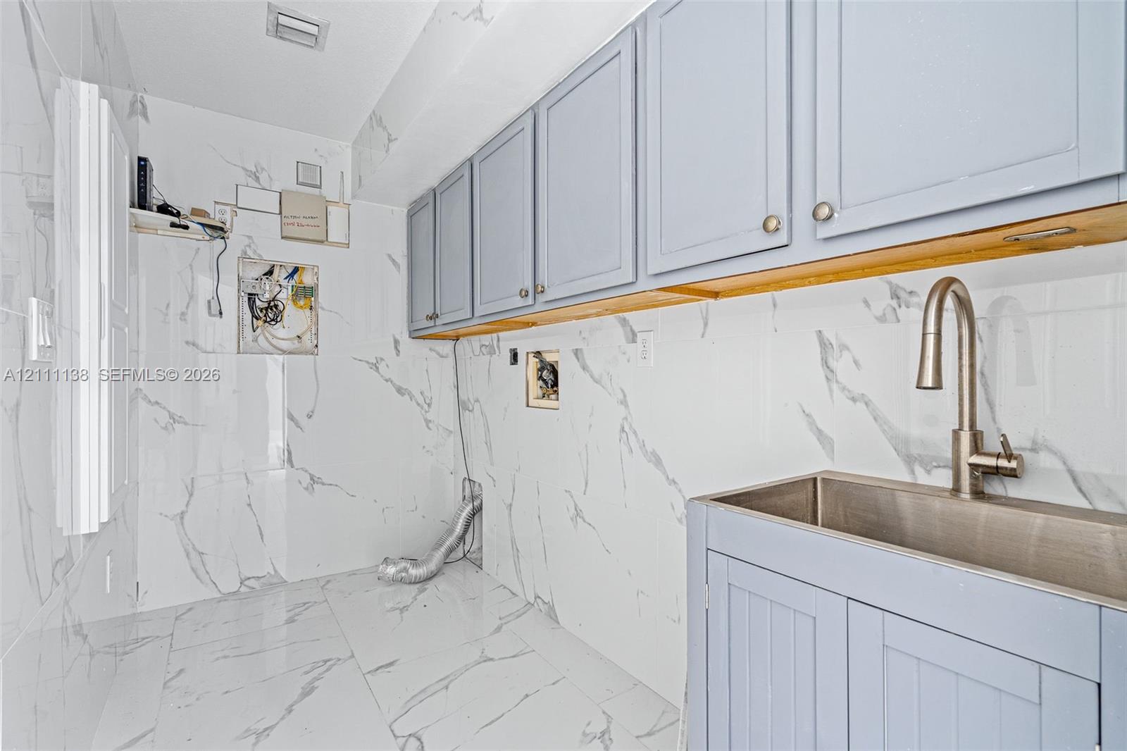 Utility area featuring floor-to-ceiling large-format stone-finish wall tile, light blue shaker-style cabinetry, a stainless steel basin sink, and a gooseneck faucet