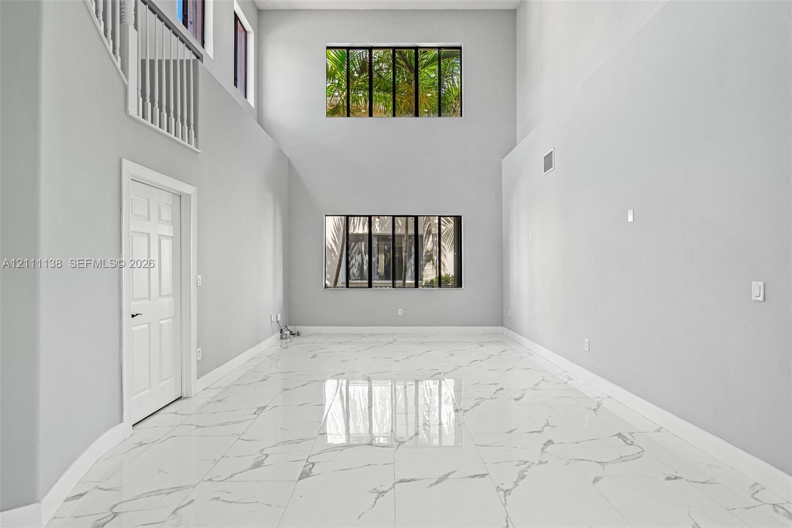 High-ceiling interior featuring polished tile flooring with marble-patterned finish, two tiers of large picture windows, and a white interior railing