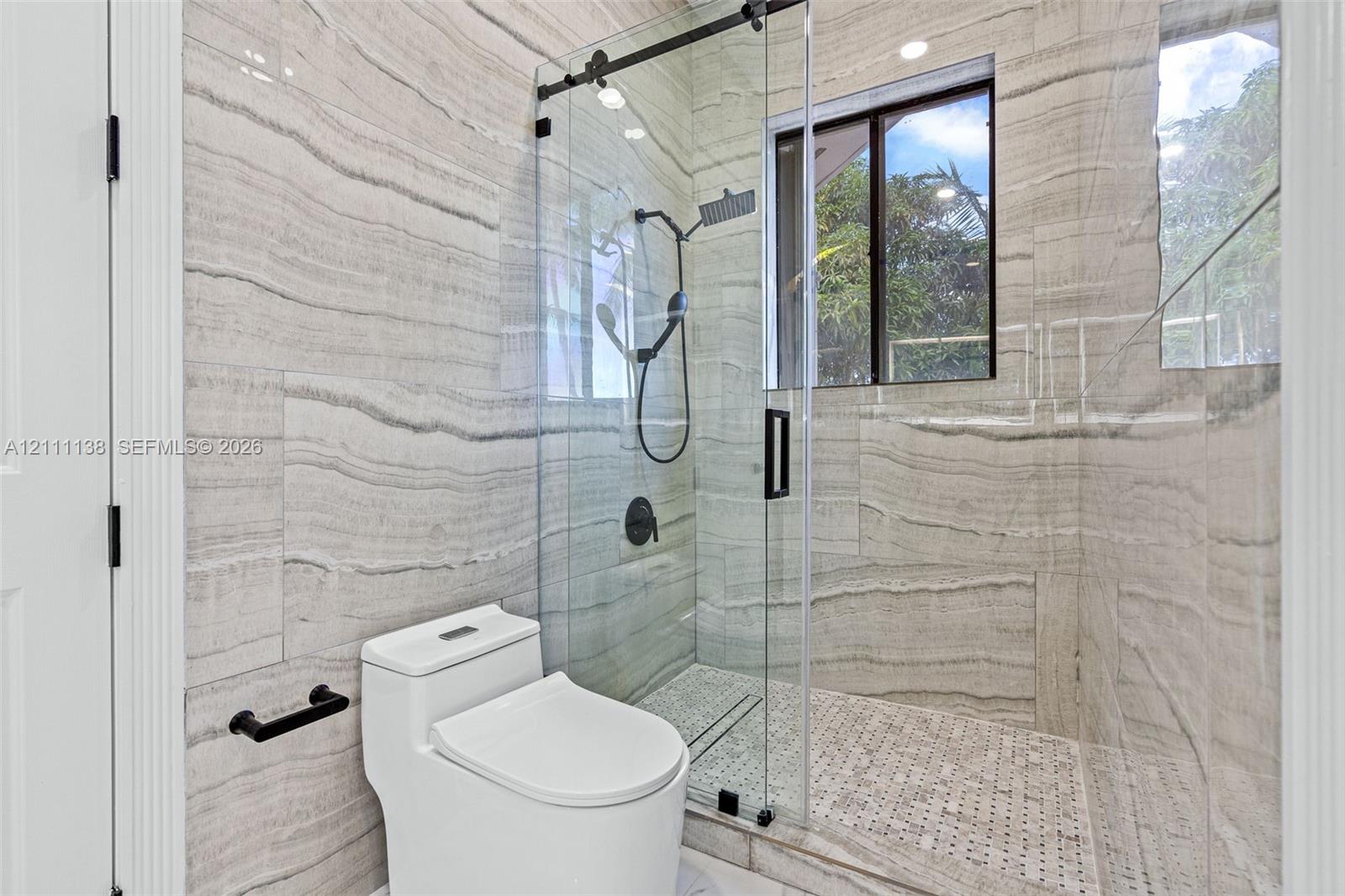 Walk-in shower featuring large-format horizontal tile, glass enclosure with matte black hardware, rainfall showerhead, and mosaic tile flooring