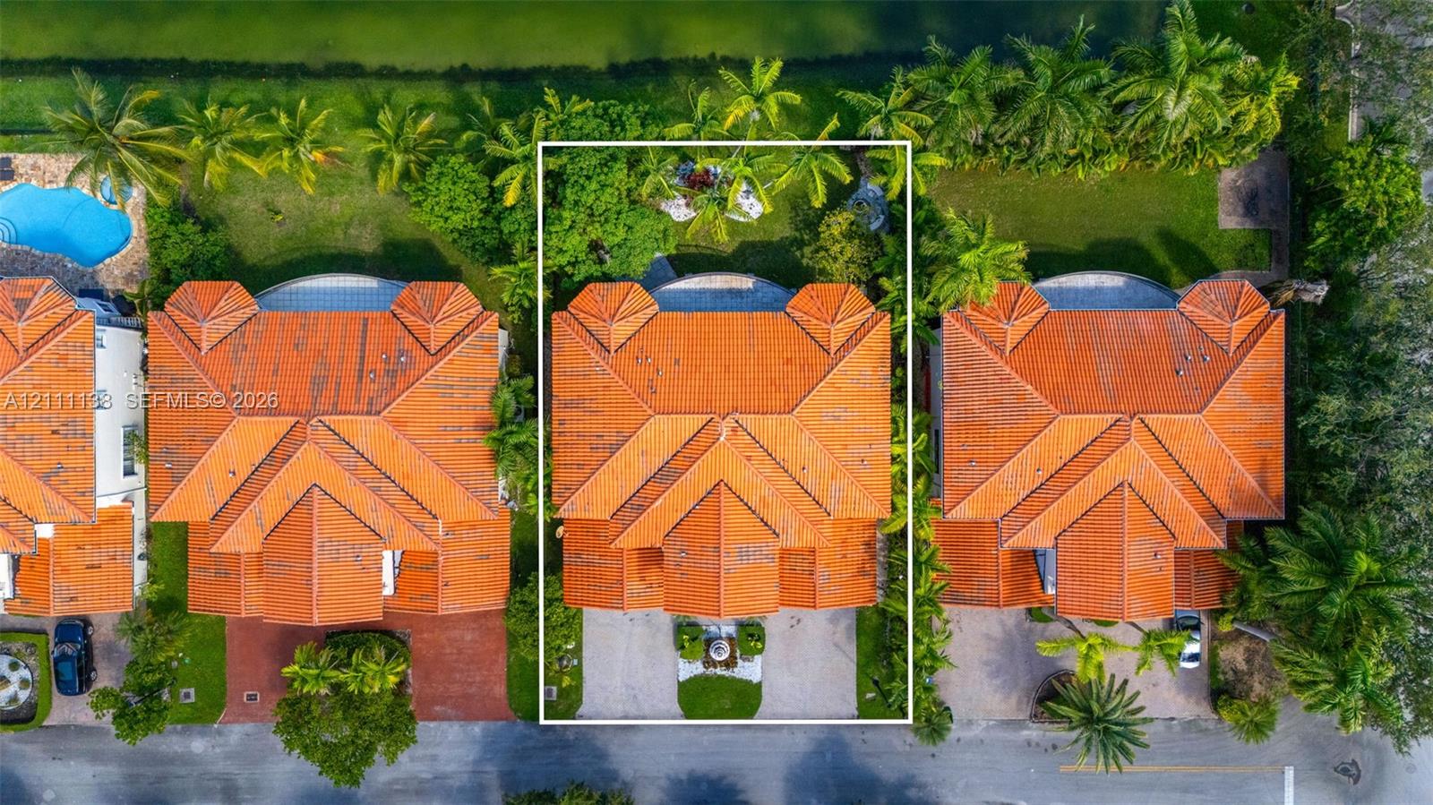 Aerial perspective featuring a tile roof, paver driveway, mature landscaping, and an expansive rear lawn