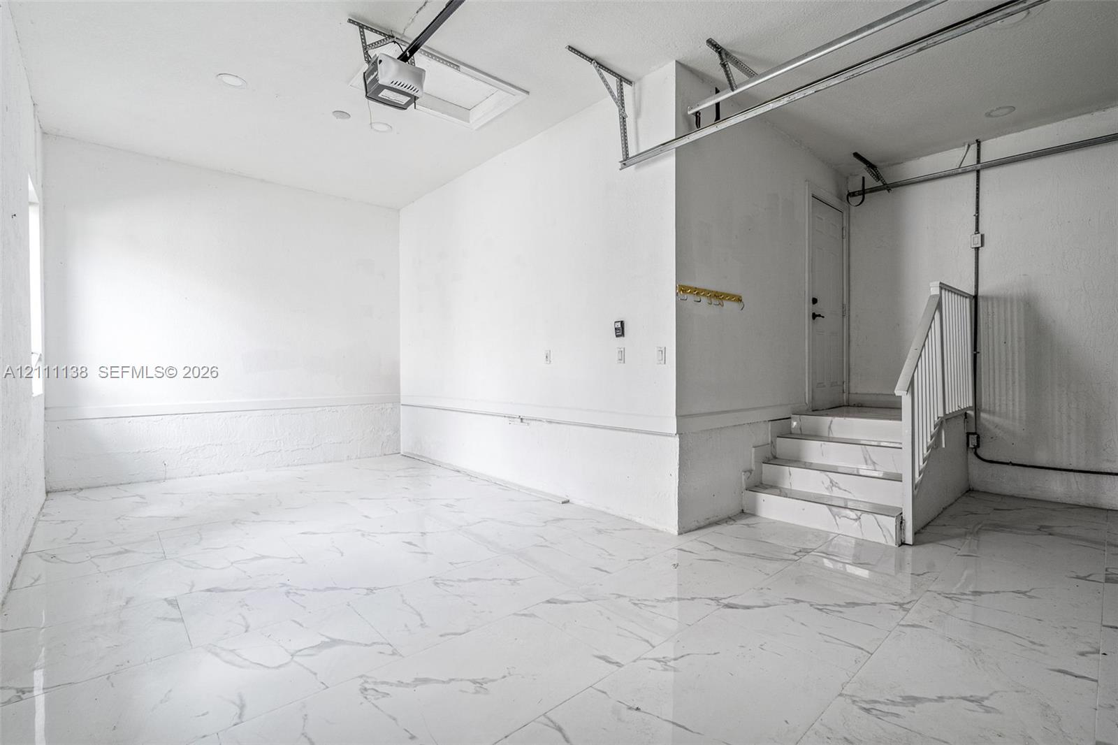 Finished garage space featuring large-format tile flooring, a staircase with matching tile risers and treads, recessed lighting, and white wall finishes