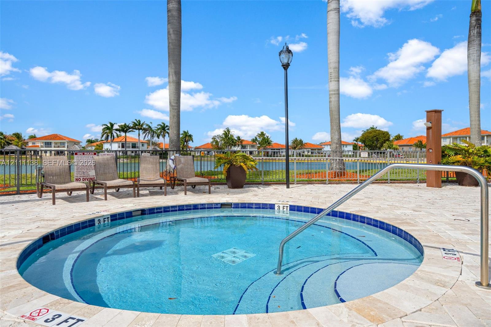 Circular spa featuring a stone-paver deck, built-in steps, a metal handrail, and a tile border