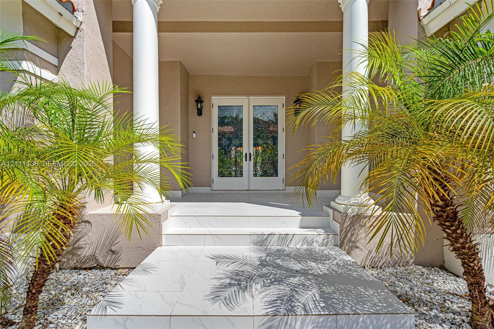 Covered entryway featuring dual white columns, stone-tile steps, glass-paned double entry doors, and wall-mounted exterior lanterns