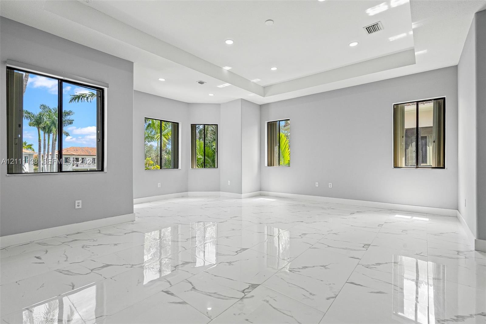 Spacious room featuring high-gloss large-format porcelain tile flooring, recessed ceiling lighting, a tray ceiling, and multiple windows