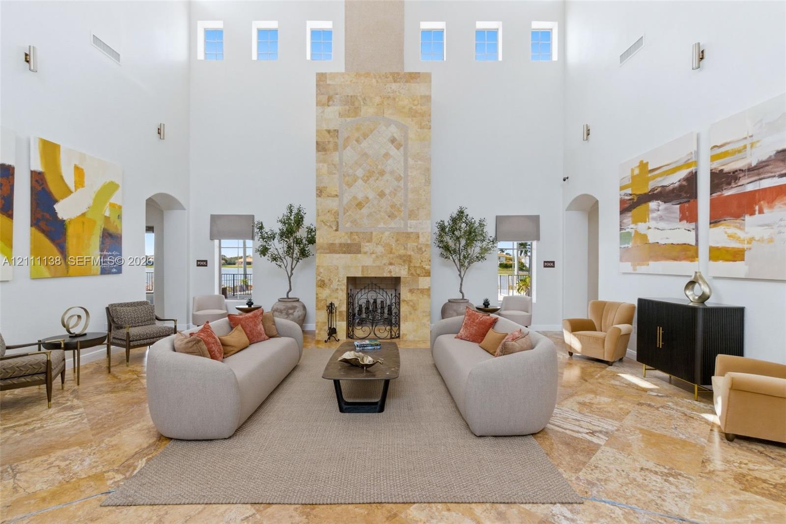 Great room featuring soaring double-height ceilings, a floor-to-ceiling stone-clad fireplace, natural stone flooring, and clerestory windows