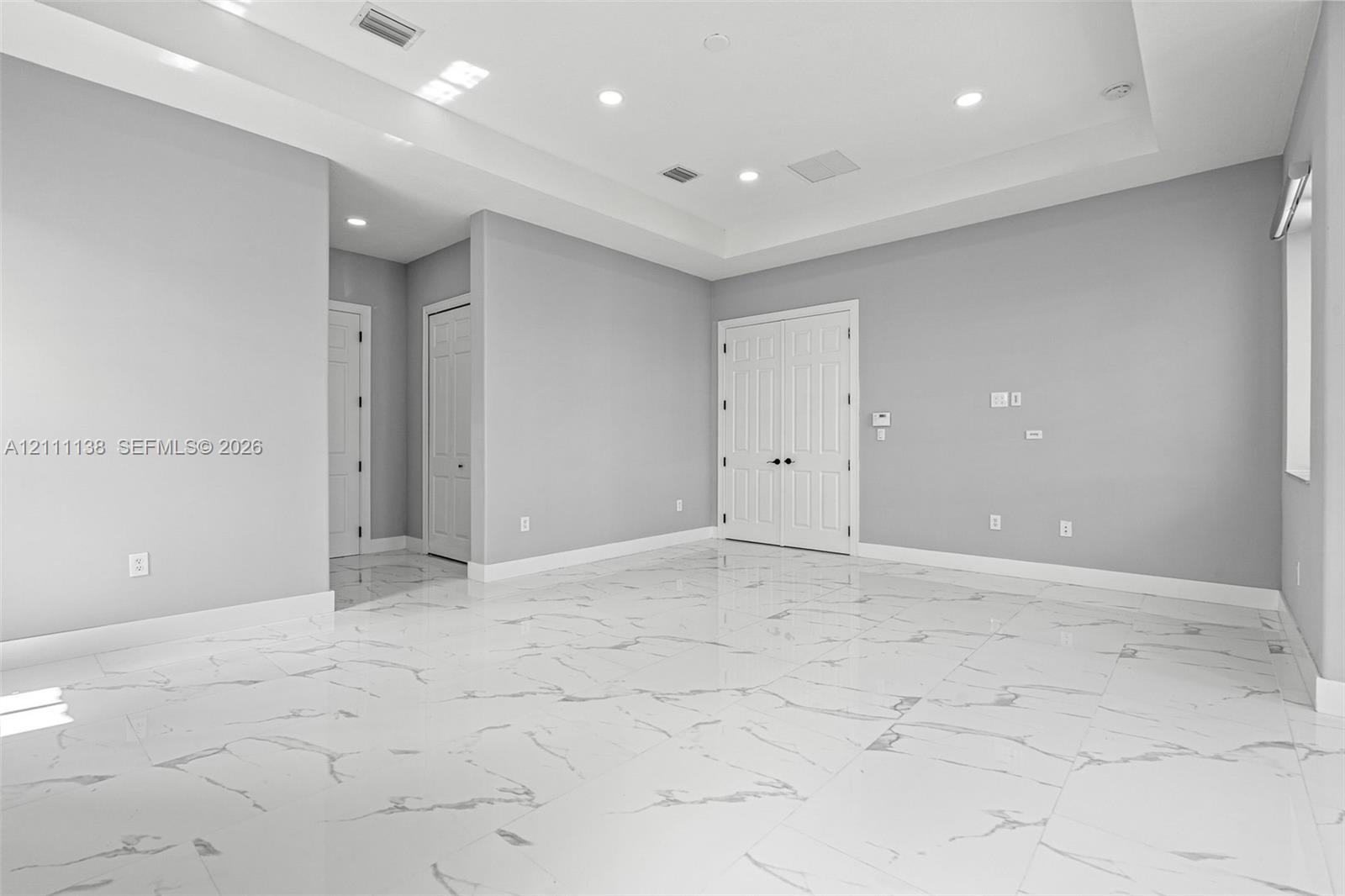Interior space featuring large-format tile flooring with marble-pattern veining, a recessed tray ceiling, recessed lighting, and double-door entry