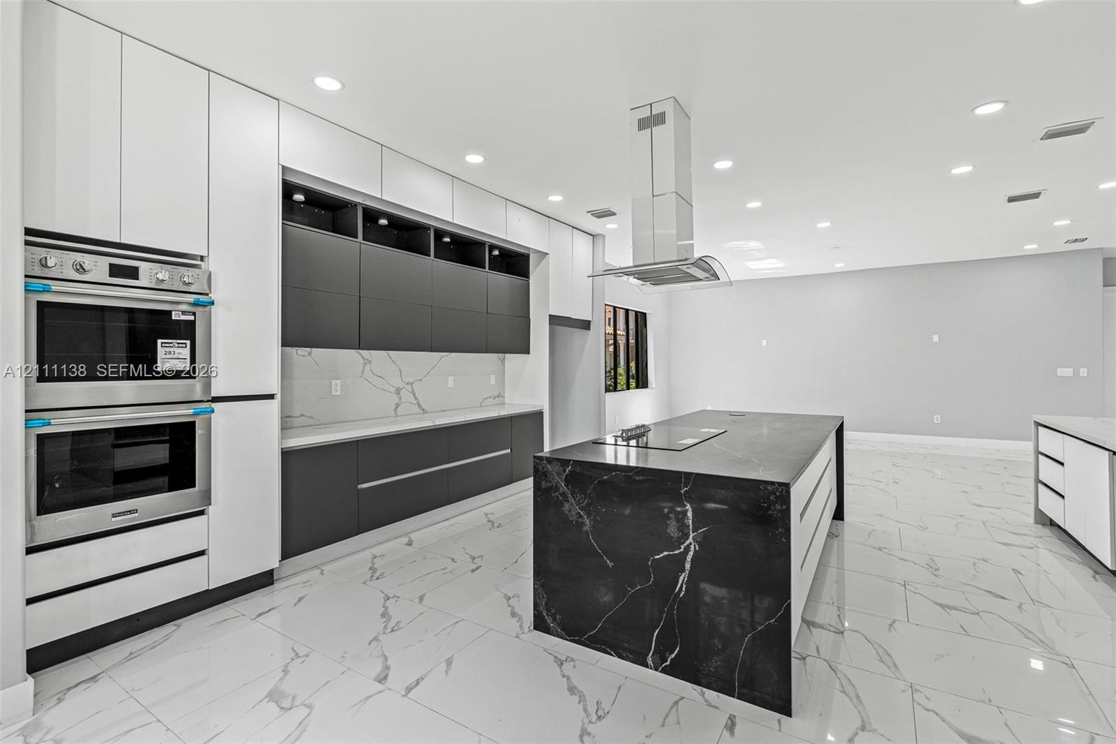 Kitchen featuring flat-panel cabinetry, a waterfall-edge island with an integrated cooktop, quartz countertops with a veined pattern, a stainless steel double wall oven, and recessed lighting