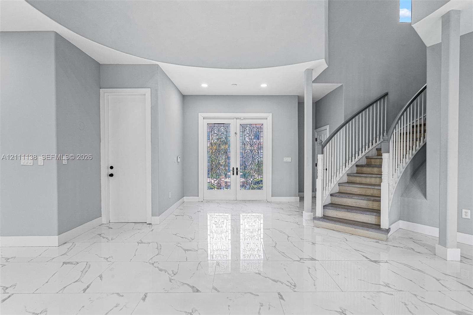 Foyer featuring large-format veined tile flooring, a curved staircase with white spindles, high ceilings with recessed lighting, and double-entry doors