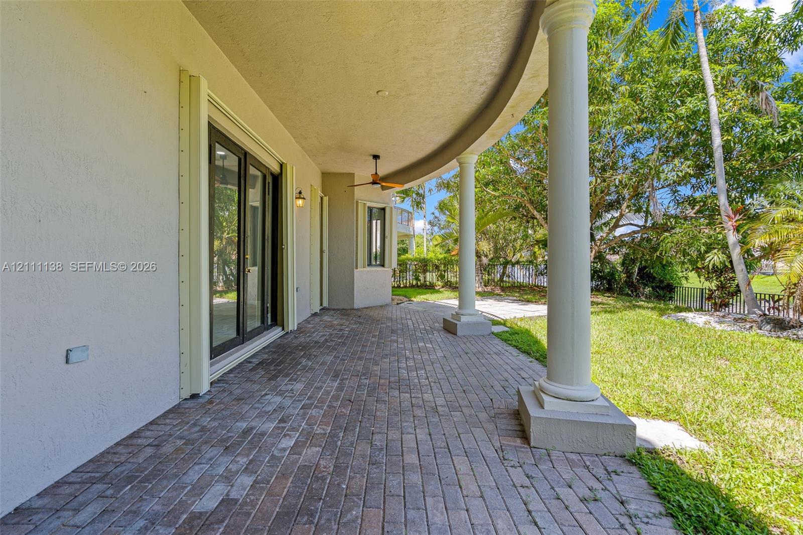 Covered curved patio featuring brick pavers, classical columns, and a ceiling-mounted fan