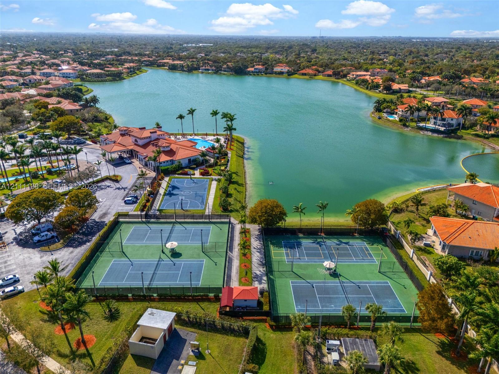 Aerial view of community recreational facilities featuring multiple tennis courts, a basketball court, and immediate waterfront access