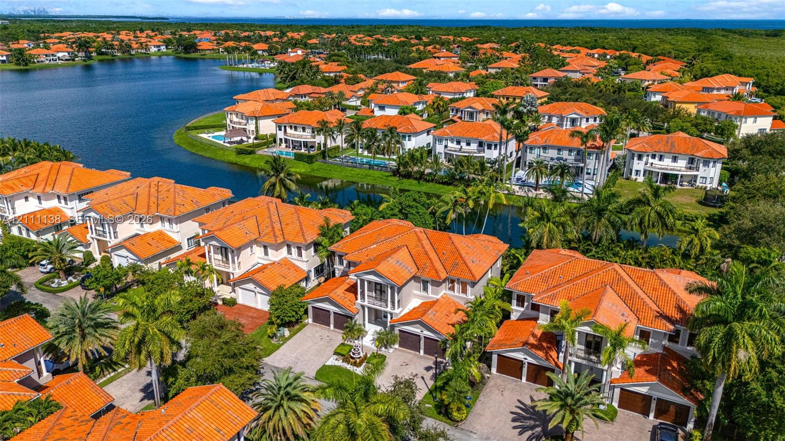 Aerial perspective featuring multi-story residences with terracotta-style tile roofing, paved driveways, multi-car garages, and mature palm landscaping situated along a waterfront canal