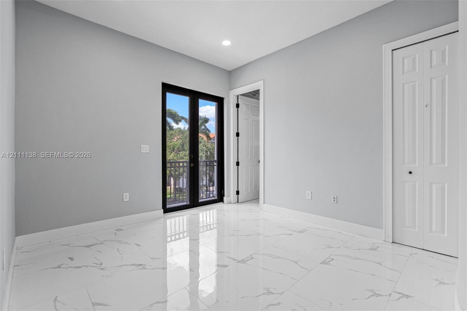 Large-format tile flooring with a veined pattern, recessed ceiling lighting, black-framed French doors, and a double-door closet with paneled detailing
