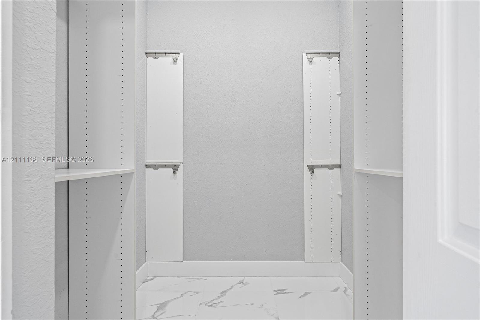 Storage space featuring white built-in shelving units, adjustable support tracks, and white stone-patterned flooring