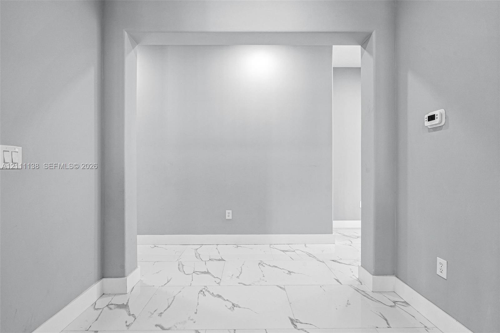 Large-format tile flooring featuring high-contrast veining, neutral grey wall paint, and a wide architectural archway