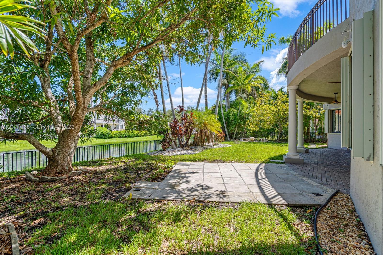 Waterfront backyard featuring a stone paver patio, a covered brick-paved terrace, column supports, and a metal balcony railing