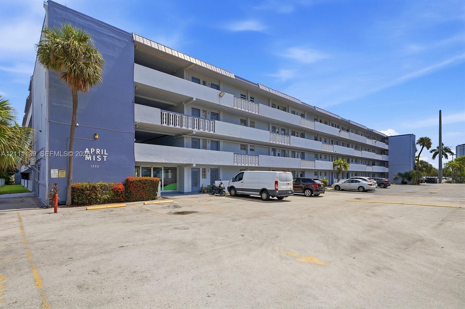 Multi-story exterior building facade with concrete construction, covered balconies, and dedicated surface parking