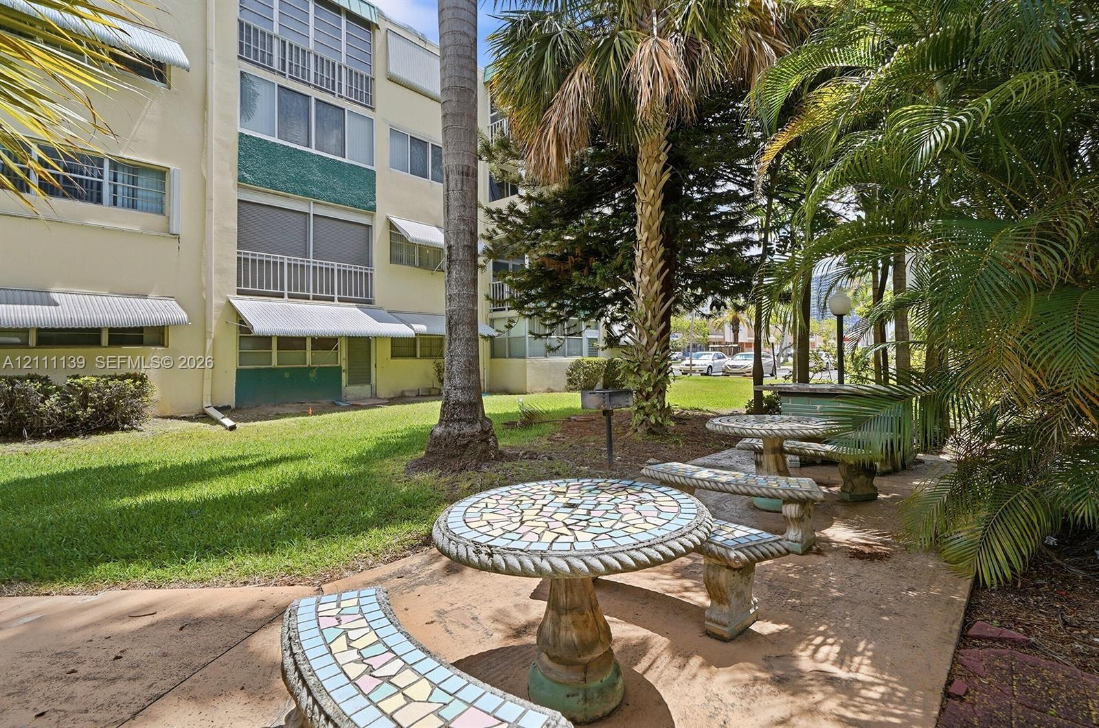 Common courtyard featuring a manicured lawn, mature palm trees, and decorative stone-tiled picnic tables with matching benches Common courtyard featuring a manicured lawn, mature palm trees, and decorative stone-tiled picnic tables with matching benches