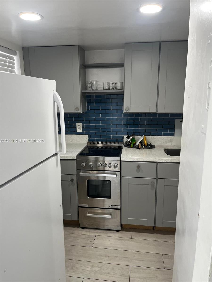 Kitchen featuring gray cabinetry, blue subway tile backsplash, light-toned stone-finish countertops, stainless steel range, and wood-finish flooring