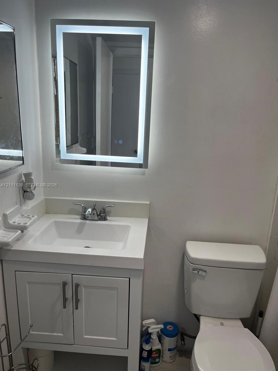 White vanity with a rectangular integrated sink, chrome dual-handle faucet, and illuminated LED-bordered mirror White vanity with a rectangular integrated sink, chrome dual-handle faucet, and illuminated LED-bordered mirror