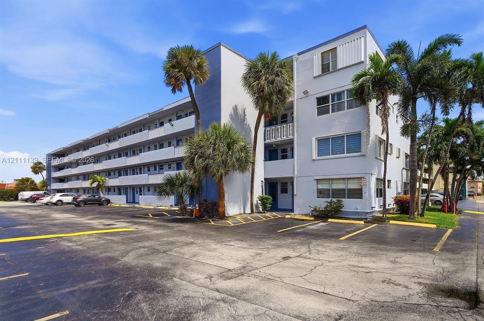 Multi-story building exterior featuring a light-toned stucco facade, tiered exterior walkways, glass windows with horizontal mullions, and mature palm trees Multi-story building exterior featuring a light-toned stucco facade, tiered exterior walkways, glass windows with horizontal mullions, and mature palm trees