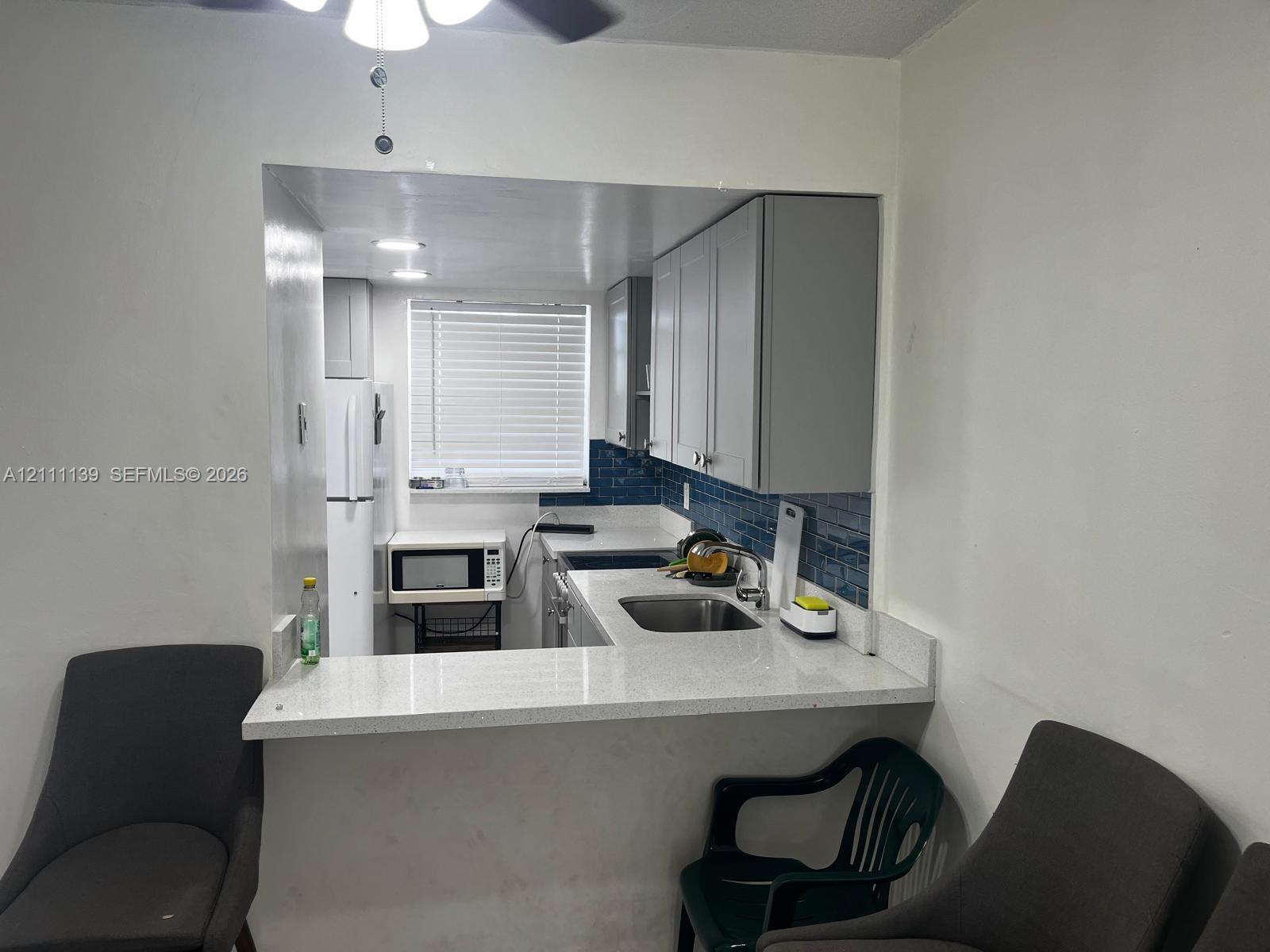 Kitchen featuring light-colored cabinetry, stone-finish countertops, a stainless steel undermount sink, blue tile backsplash, and a breakfast bar