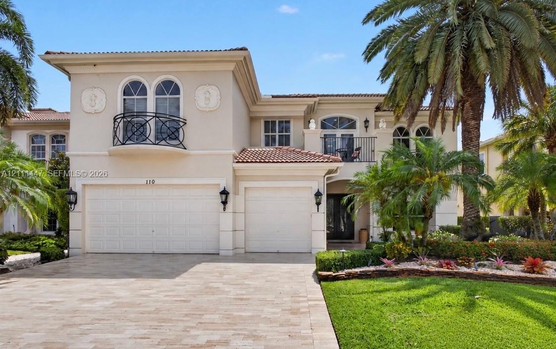 Two-story stucco exterior featuring arched windows, wrought-iron balconies, a tile roof, and a multi-car garage with paver driveway Two-story stucco exterior featuring arched windows, wrought-iron balconies, a tile roof, and a multi-car garage with paver driveway