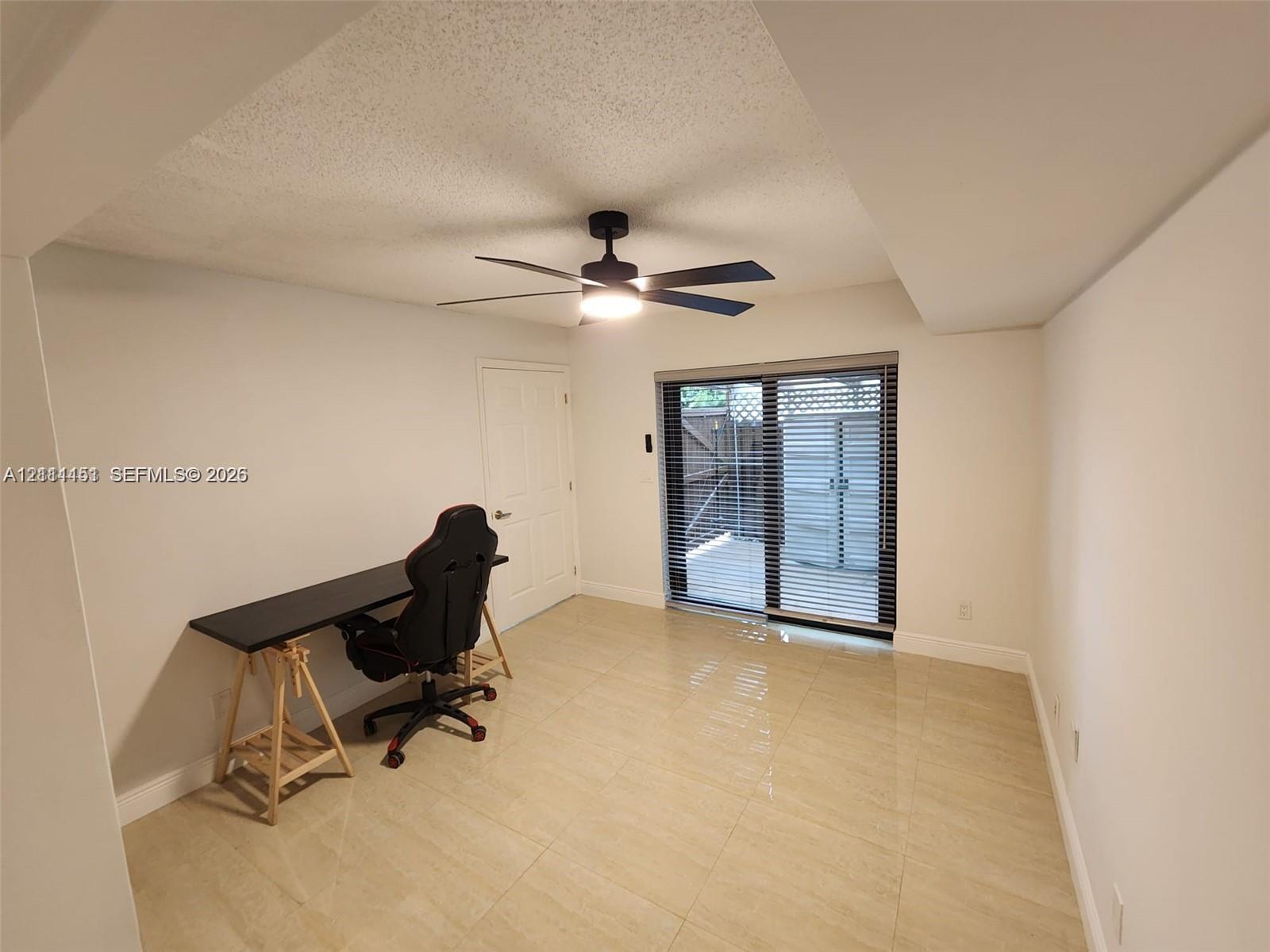 Interior space featuring large-format tile flooring, matte black ceiling fan with integrated lighting, and sliding glass doors with window blinds