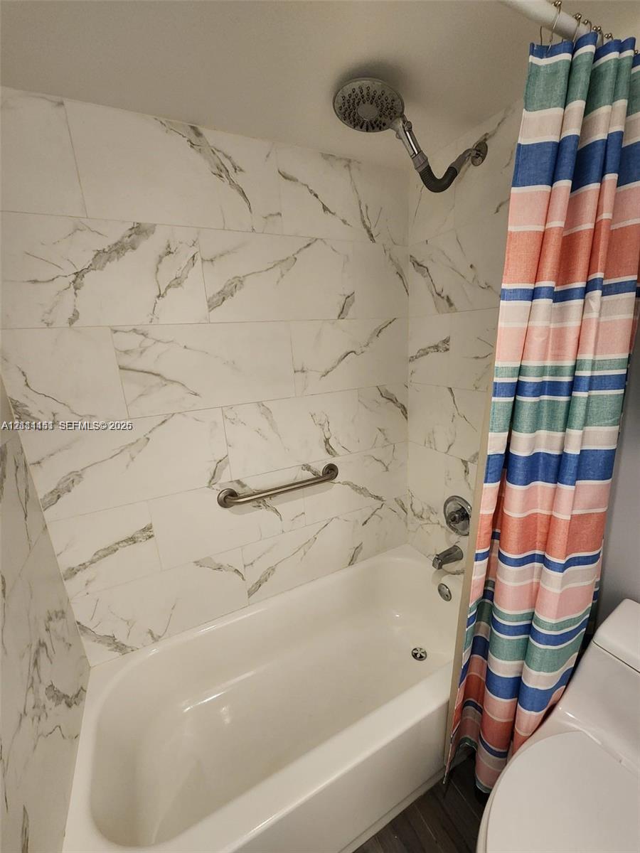 Full-height wall tiling with a veined pattern, brushed nickel shower head, built-in grab bar, and soaking tub