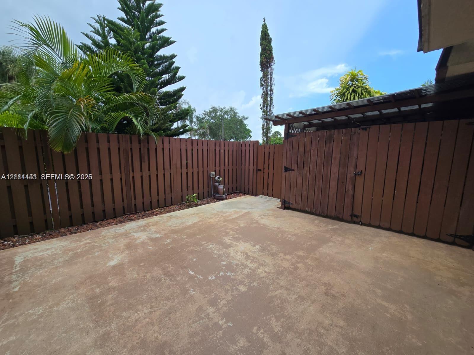 Private patio area enclosed by wood fencing, featuring a concrete surface and a covered storage structure Private patio area enclosed by wood fencing, featuring a concrete surface and a covered storage structure