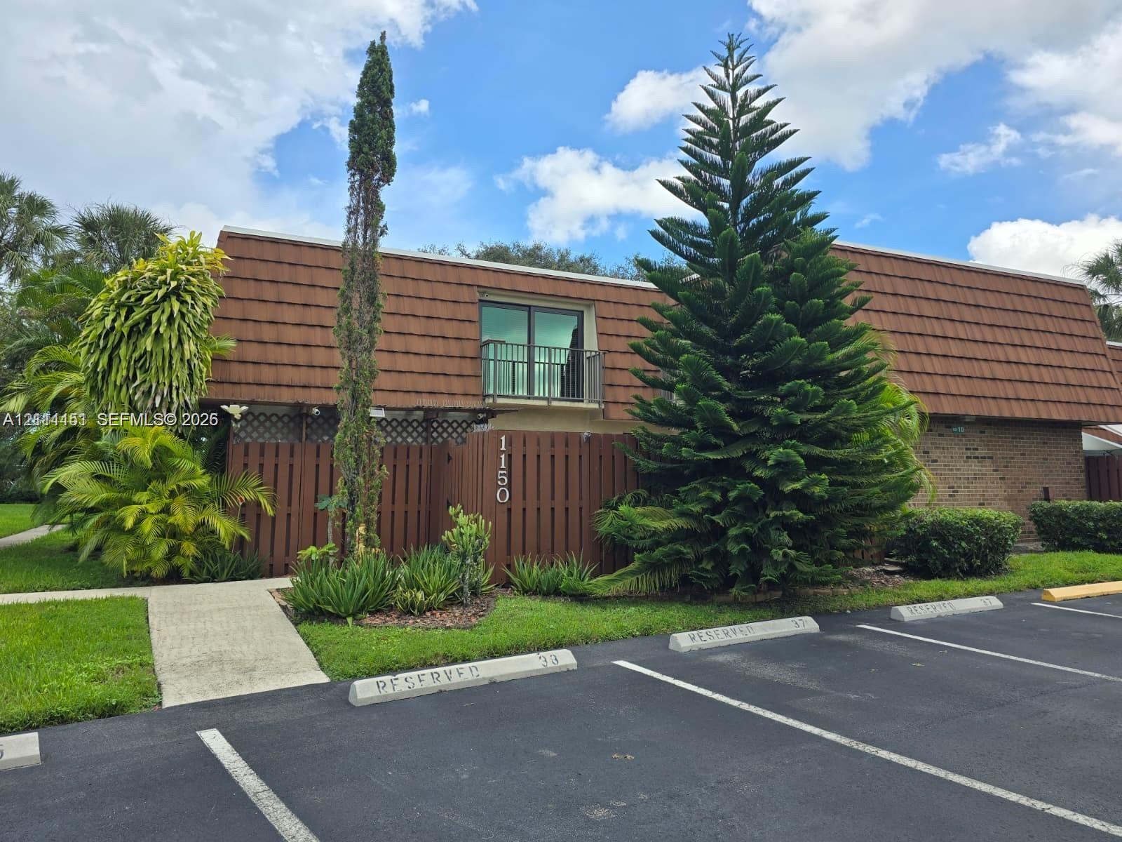 Exterior facade featuring a mansard-style roof, brick masonry, a wooden privacy fence, and a second-story balcony with metal railing Exterior facade featuring a mansard-style roof, brick masonry, a wooden privacy fence, and a second-story balcony with metal railing