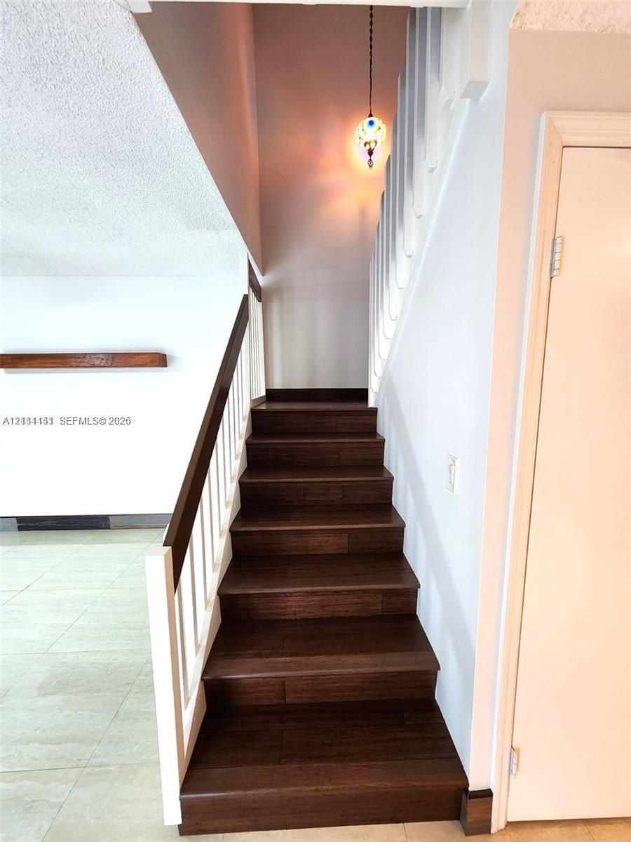 Staircase featuring wood-finish treads, a white handrail, a decorative glass pendant light, and a floating wood-finish shelf