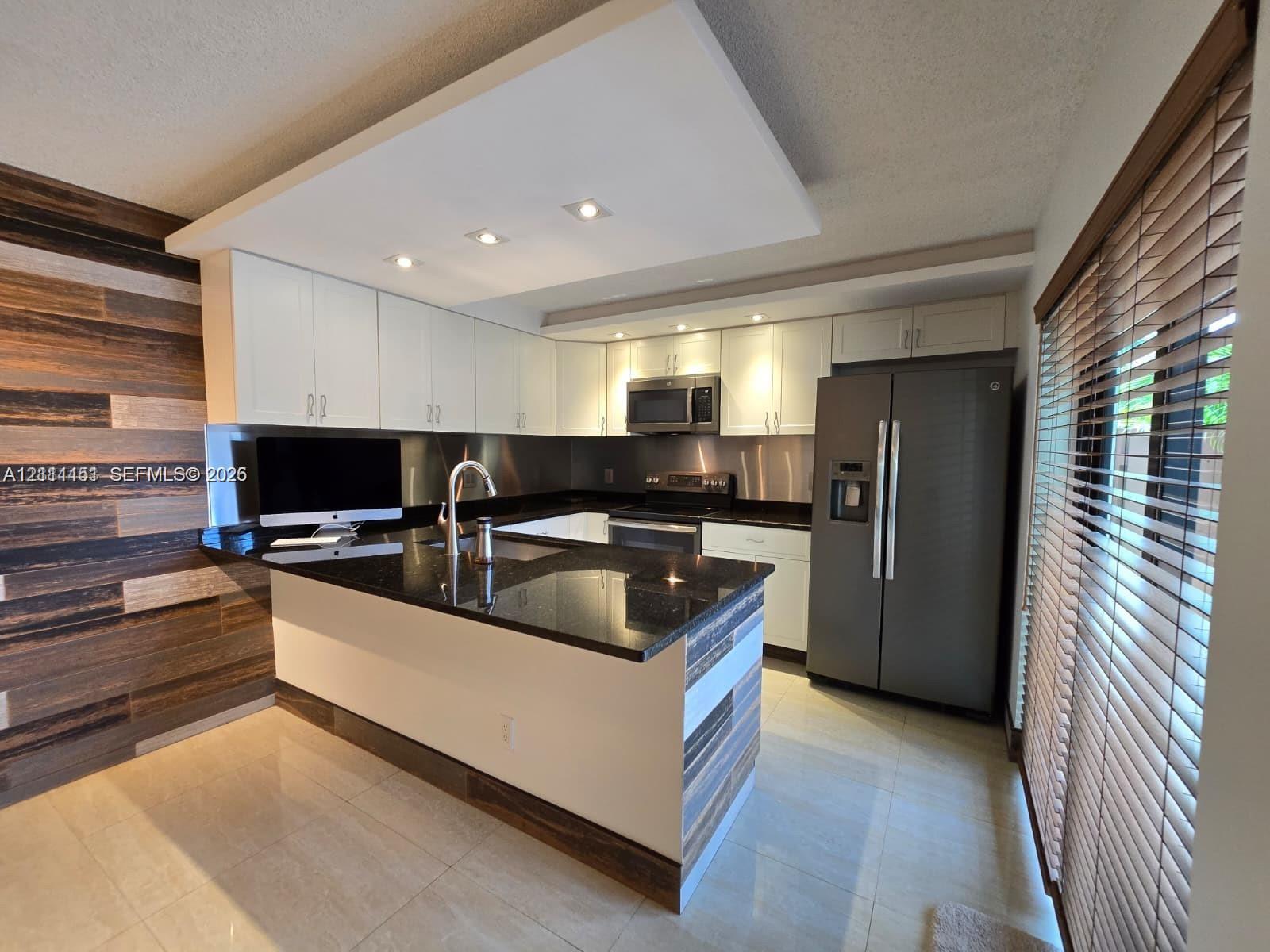 Kitchen featuring white shaker-style cabinetry, dark stone countertops, stainless steel appliances, recessed ceiling lighting, and horizontal wood-panel accent wall Kitchen featuring white shaker-style cabinetry, dark stone countertops, stainless steel appliances, recessed ceiling lighting, and horizontal wood-panel accent wall