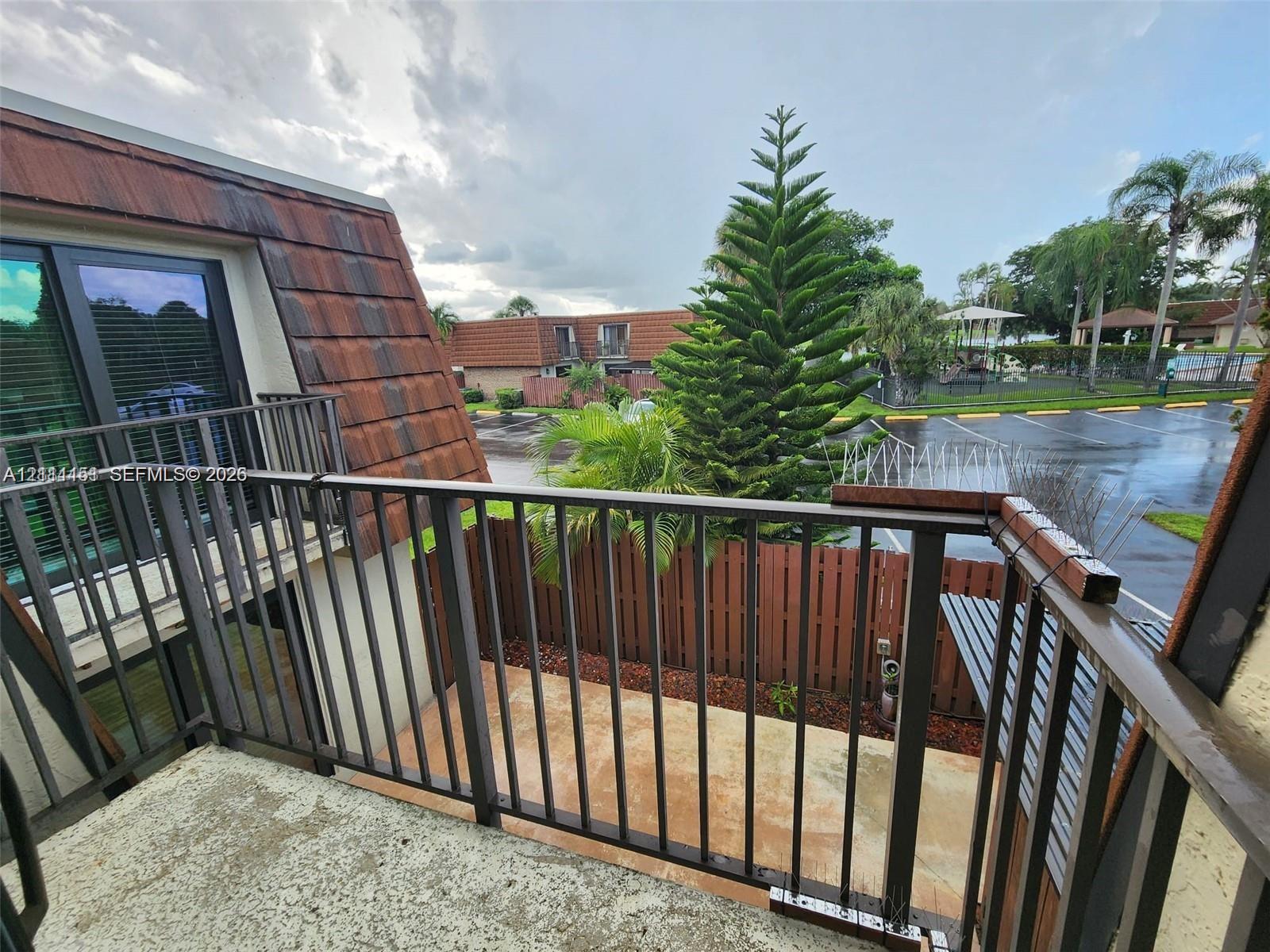 Private balcony featuring metal railings, textured concrete flooring, and an architectural mansard roofline