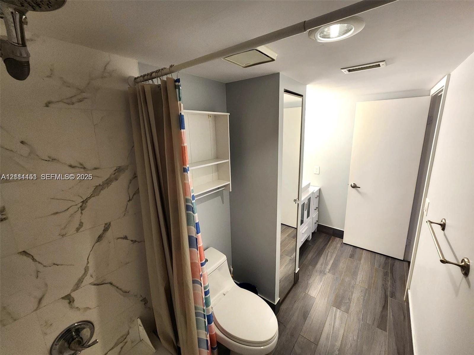 Bathroom featuring shower surround with large-format stone-patterned tile, wood-finish flooring, white vanity, built-in wall shelving, and inset ceiling lighting