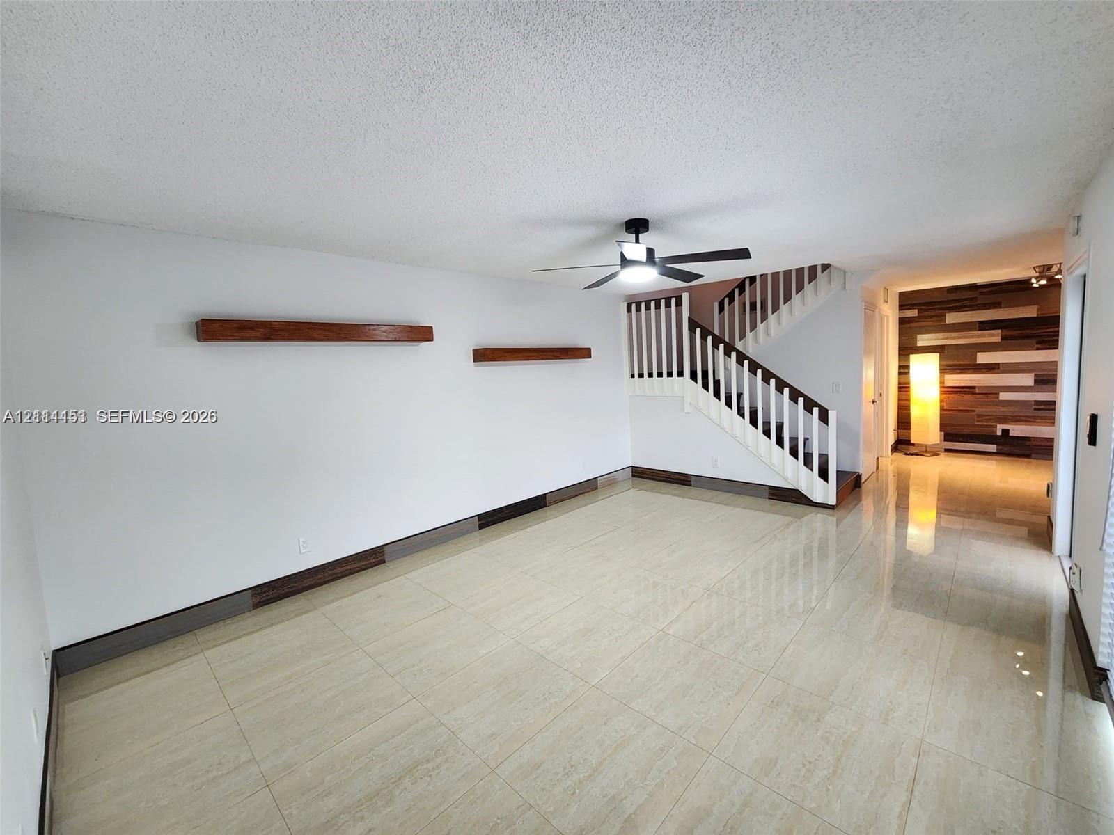 Interior space featuring polished tile flooring, wall-mounted wood-finish shelving, an integrated staircase with a white balustrade, and a decorative multi-tonal wood panel accent wall