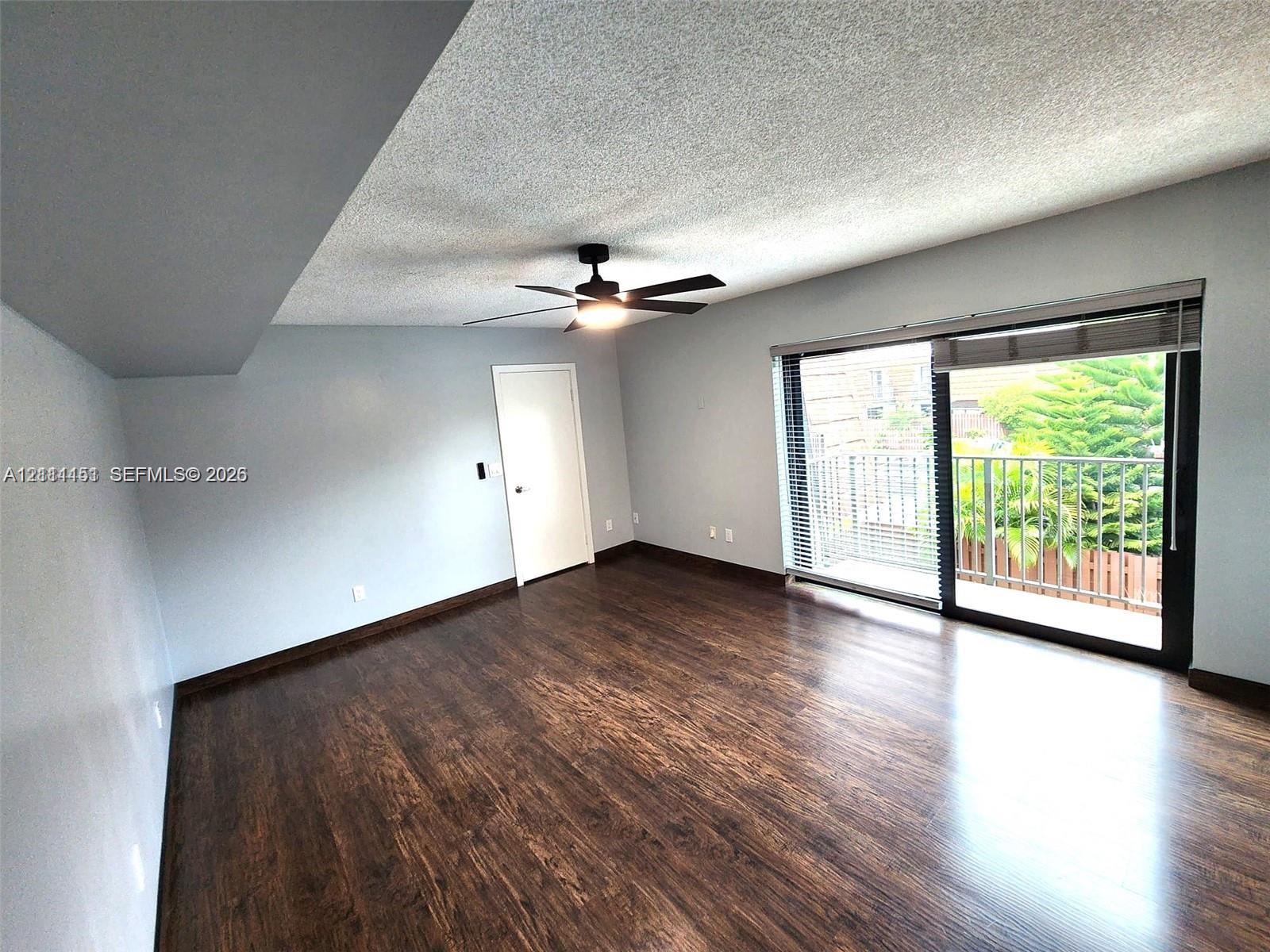 Room featuring wood-finish flooring, a ceiling fan with integrated lighting, and a large sliding glass door opening to an exterior balcony
